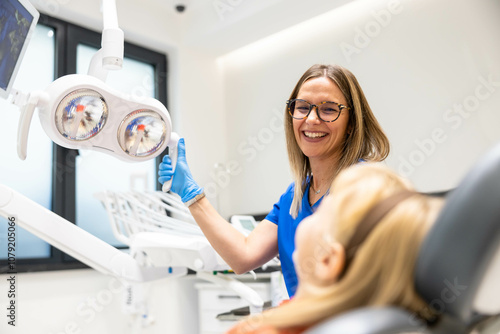 Картината върху платно A dentist wearing glasses and gloves interacts with her young patient in a modern and brightly lit dental clinic, emphasizing care and professionalism