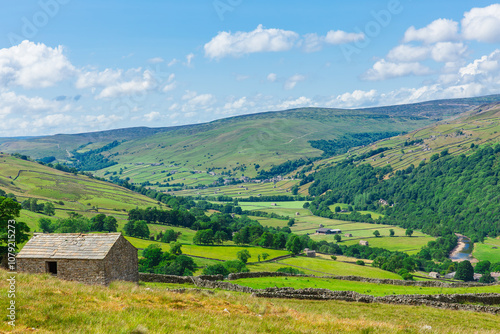 The beautiful dale of Swaledale in Summer time, Yorkshire Dales, UK with sweeping fells, green meadows, drystone walling m stone barns or cow houses and the River Swale. Horizontal, Space for copy. photo