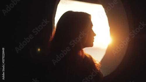 Atmospheric, cinematic video of a girl looking into the golden sunset near a round window, sun rays, beauty, love, calm, melancholy, pleasure, face portrait, life, moment, alive, feelings, deep