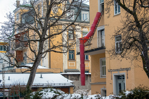 Salzburg, Austria - 01.13.2024: Hanging sections of a red construction waste chute on the facade of a historic building. photo