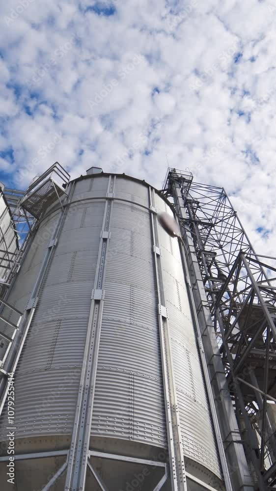Modern industrial grain elevators for grain storage. Steel silos for storing grain on a agricultural farm against beautiful sky background. Close-up. Vertical video Modern industrial grain elevators for grain storage. Steel silos for storing grain on a agricultural farm against beautiful sky background. Close-up. Vertical video