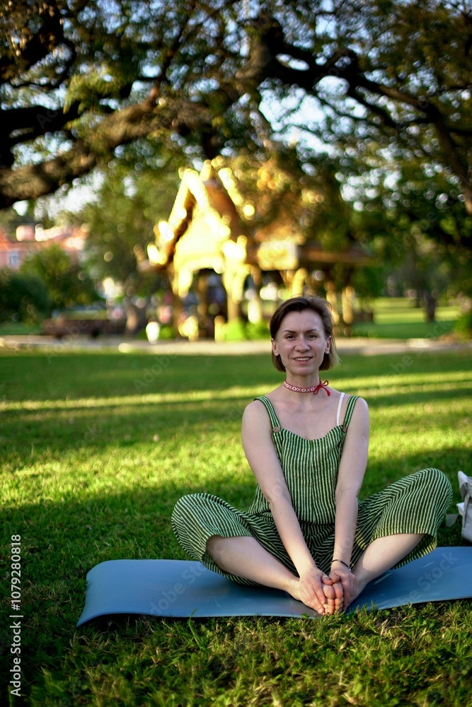 woman doing exercises in the park. a young woman of European appearance sits in the lotus position on a blue rug in a city park. Yoga. woman doing exercises in the park. a young woman of European appearance sits in the lotus position on a blue rug in a city park. Yoga.