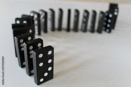 lined up standing black dominoes isolated on white background metaphor for cause and effect, fate, causality, fallen, chain reaction, predictability business backdrop photo