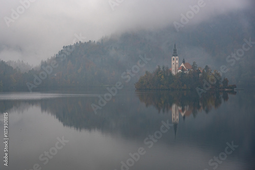 Assumption of mary pilgrimage church Lake bled island reflecting on calm water during foggy autumn day