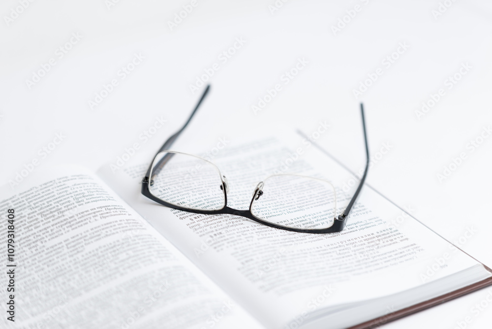 Glasses resting on open book with text, symbolizing reading, research, science, and law study, representing focused exploration of knowledge and academic or legal studies Glasses resting on open book with text, symbolizing reading, research, science, and law study, representing focused exploration of knowledge and academic or legal studies