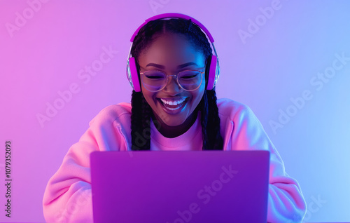 Young woman enjoys music while working on a laptop in colorful lighting photo