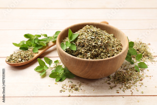 Dried oregano in bowl, spoon and green leaves on wooden table