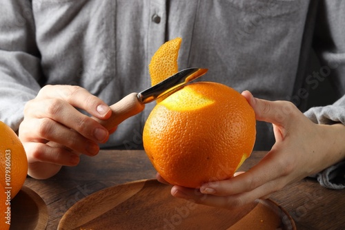 Woman zesting orange at wooden table, closeup