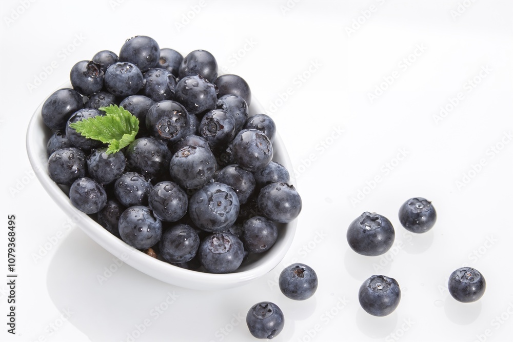 Fresh blueberries in white bowl with mint leaf on white background Fresh blueberries in white bowl with mint leaf on white background