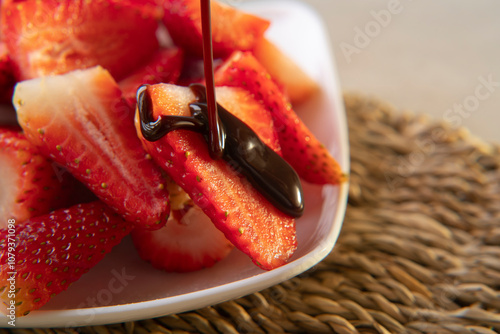 Close up of chocolate dripping onto a strawberry on a white square plate with chopped strawberries