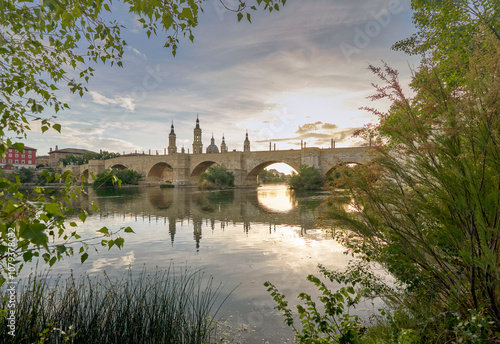 View on the Stone Bridge and Basilica of Our Lady of the Pillar on the banks of Ebro river at sunset. Zaragoza, Spain