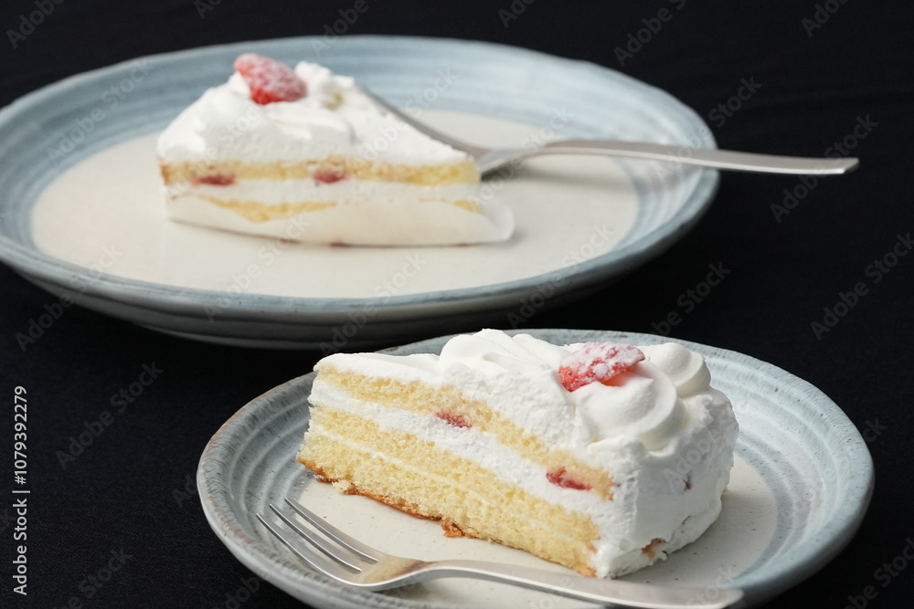 A small Japanese strawberry shortcake and a fork each on two stylish Japanese-style large and small plates on a black cloth on a white table A small Japanese strawberry shortcake and a fork each on two stylish Japanese-style large and small plates on a black cloth on a white table