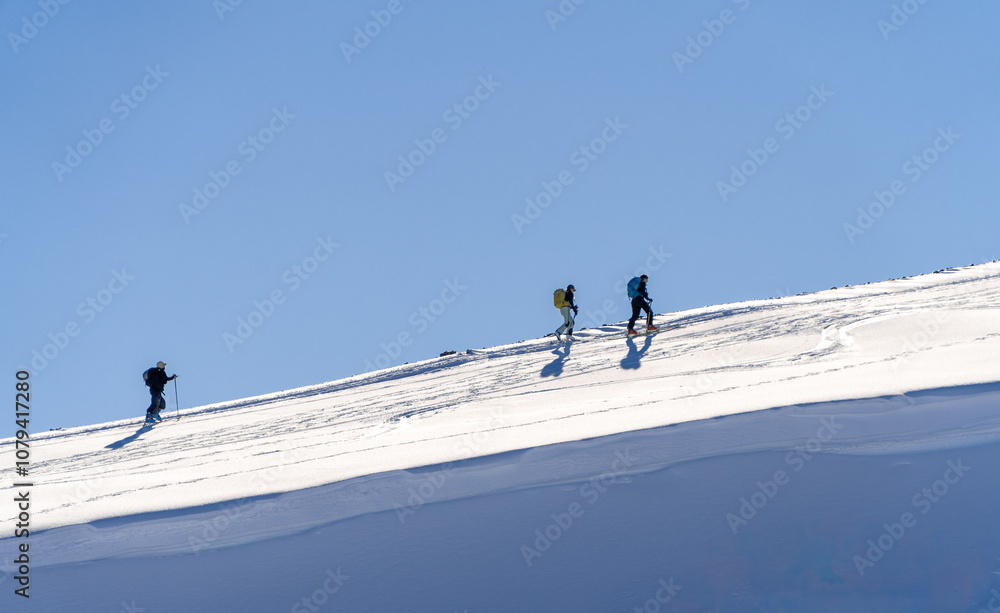 Hikers Trekking Across Snowy Slope Under Clear Blue Sky