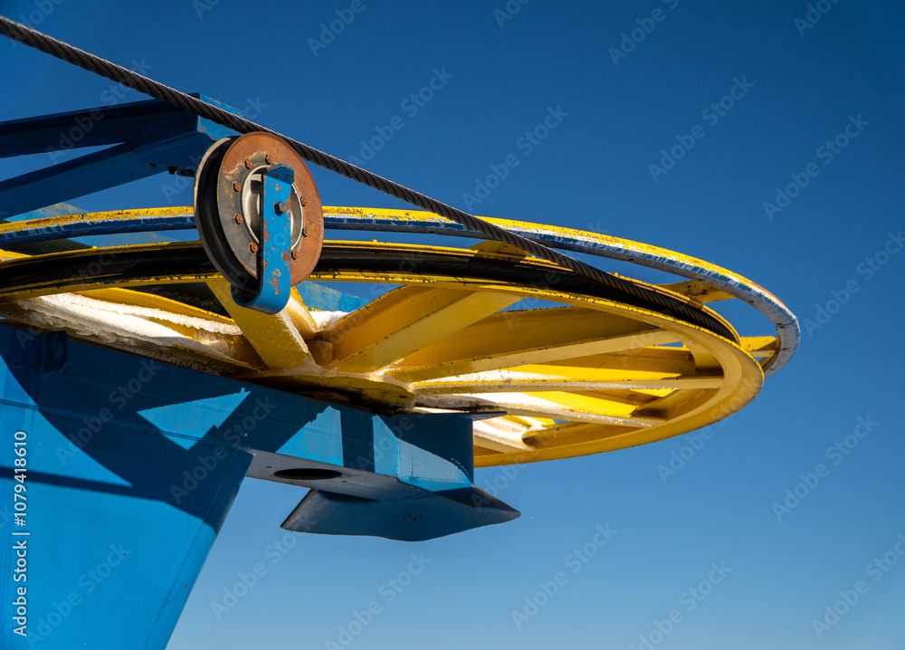 Close-up view of a colorful ski lift pulley mechanism in blue and yellow, set against a clear blue sky.