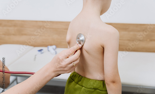 Doctor uses stethoscope to check childs back during routine health examination photo