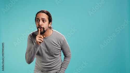 Portrait of man doing shushing hand gesturing, requesting silence. Person placing finger on lips, doing quiet sign gesture, asking for secrecy, isolated over studio background, camera B photo