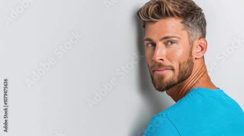 A confident man with a beard in a volunteer tshirt poses effortlessly against a white backdrop, exuding calm charm.