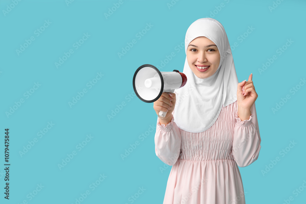 Young Asian Muslim woman with megaphone pointing at something on blue background. National Be Heard Day Young Asian Muslim woman with megaphone pointing at something on blue background. National Be Heard Day