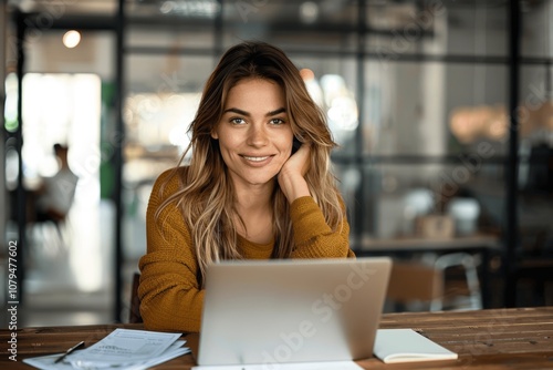 Happy professional businesswoman using laptop in office, smiling executive working at desk with papers and notebook, female entrepreneur in corporate environment