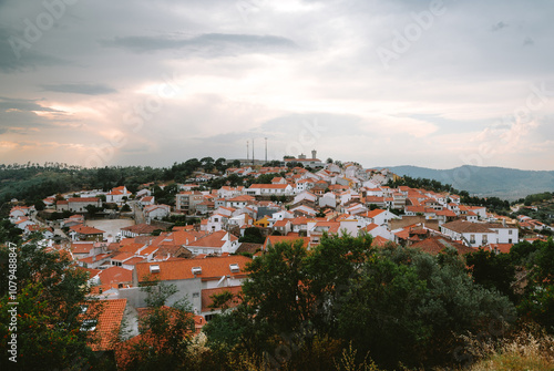 Charming village of penamacor on hill with terracotta roofs and whitewashed walls, surrounded by green hills under dramatic cloudy sky