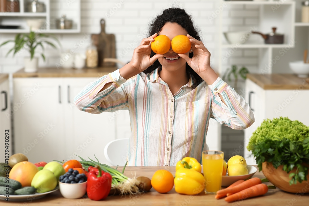 Young happy African-American woman with glass of juice, different vegetables and fruits in kitchen. Independence from Meat Day Young happy African-American woman with glass of juice, different vegetables and fruits in kitchen. Independence from Meat Day