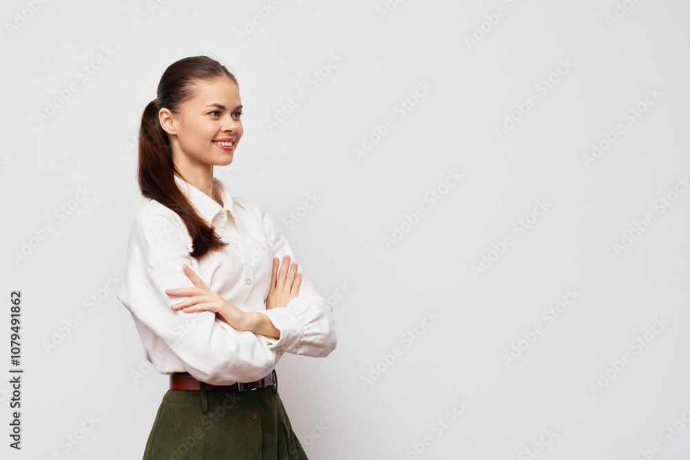 Woman in a white blouse with arms crossed, smiling, standing against a light gray background, conveying confidence and positivity in a professional setting Woman in a white blouse with arms crossed, smiling, standing against a light gray background, conveying confidence and positivity in a professional setting