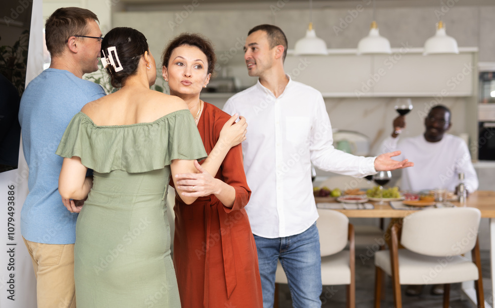 Smiling woman, hostess of house, greetingly hugging and kissing female friend, enjoying convivial dinner party atmosphere at home.. Smiling woman, hostess of house, greetingly hugging and kissing female friend, enjoying convivial dinner party atmosphere at home..