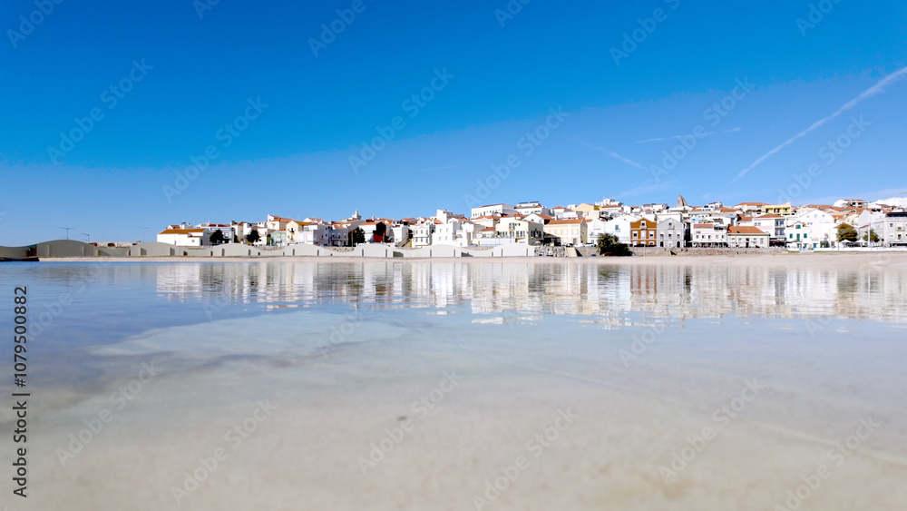 A picturesque coastal town with whitewashed buildings reflects on the calm waters of a lagoon A picturesque coastal town with whitewashed buildings reflects on the calm waters of a lagoon