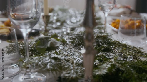 Close up view of festive dining table adorned with pine branches, eycalyptus leaves, glass beads, elegant glassware and silver candle holders for Christmas celebration photo