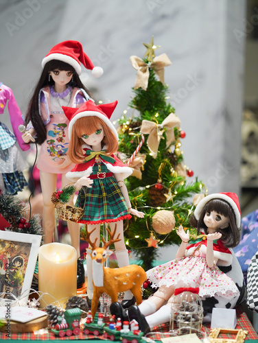 Merry Christmas. A cute doll display for Christmas party decoration. including 3 girls wearing Santa's hat and the Christmas tree on the background. Selective focus on the girl with green eyes.
