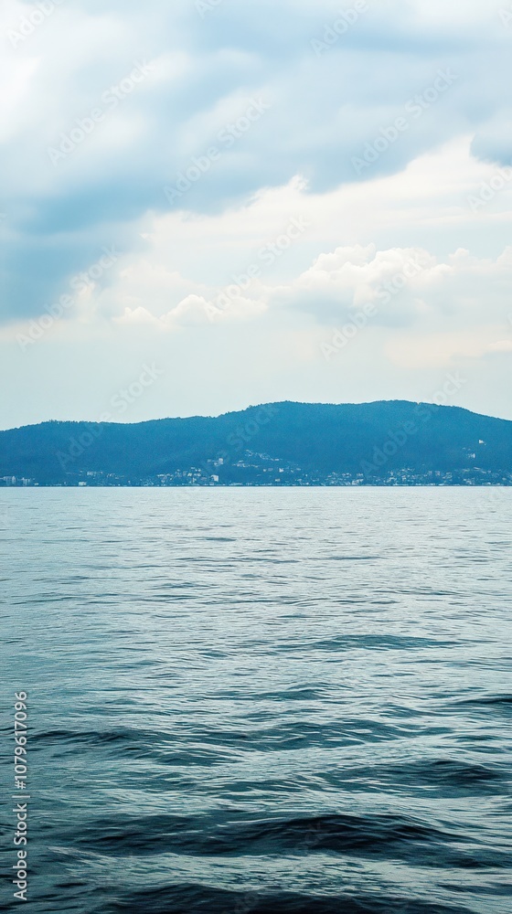 Obraz premium A serene view of calm waters reflecting a cloudy sky and distant hills.