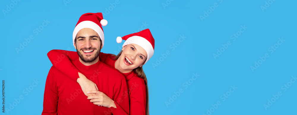 Happy Holidays. Cheerful Smiling Young Couple In Santa Hats Posing On Blue Background, Joyful Loving Man And Woman Wearing Red Sweaters Posing At Camera Together, Enjoying Xmas Mood, Copy Space Happy Holidays. Cheerful Smiling Young Couple In Santa Hats Posing On Blue Background, Joyful Loving Man And Woman Wearing Red Sweaters Posing At Camera Together, Enjoying Xmas Mood, Copy Space