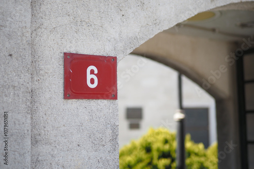 A prominently displayed number 6 sign affixed to a concrete wall, adorned with greenery photo