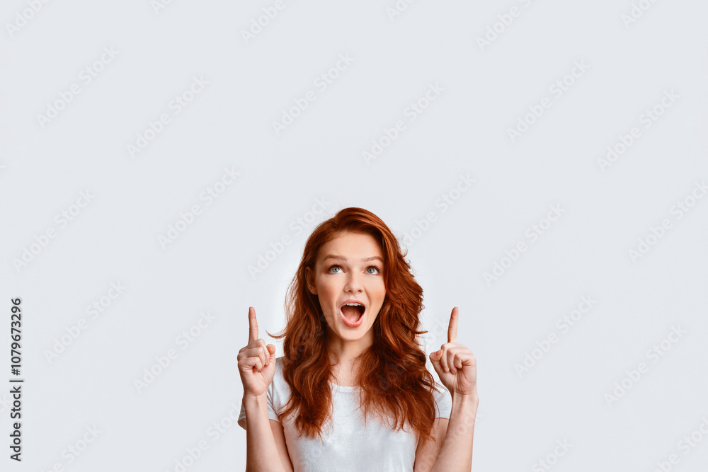 Look Up. Red-Haired Teen Girl Pointing Fingers Upward At Free Space Posing Over White Background. Studio Shot Look Up. Red-Haired Teen Girl Pointing Fingers Upward At Free Space Posing Over White Background. Studio Shot