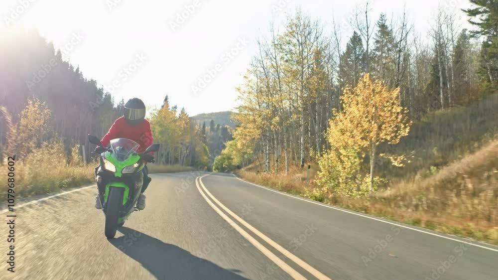 Motorcyclist riding down beautiful autumn canyon road with sun flare Motorcyclist riding down beautiful autumn canyon road with sun flare