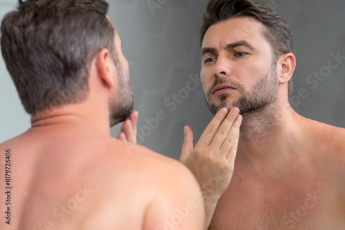 Sexy sensual man with perfect skin touch face after shaving. Skin care healthcare cosmetic procedures concept. Close up man looking in mirror, sensitive skin, cosmetology treatment. Skin care. photo