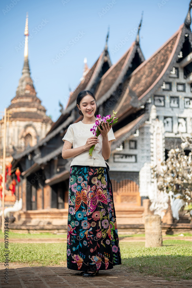 Obraz premium A charming Asian woman with a temple in the background, admiring a flower bouquet in her hand.