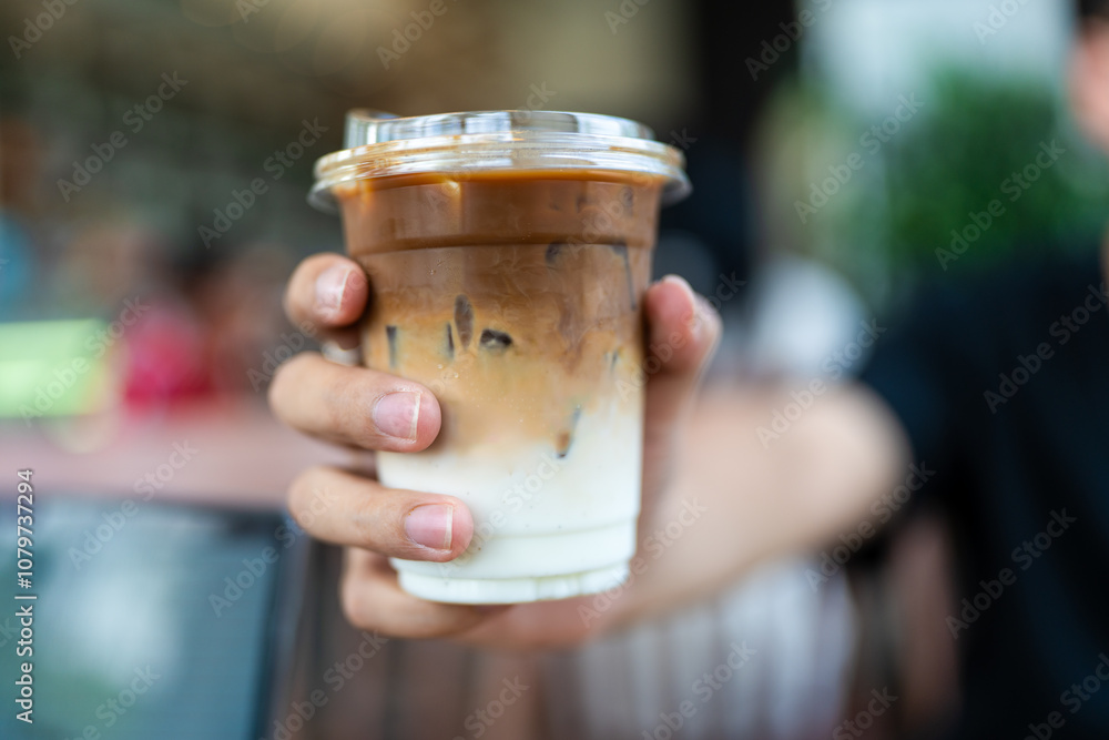 Man holds a plastic glass of iced coffee latte, upper layer is shot of esspeso lower is fresh milk, selective focus. Man holds a plastic glass of iced coffee latte, upper layer is shot of esspeso lower is fresh milk, selective focus.
