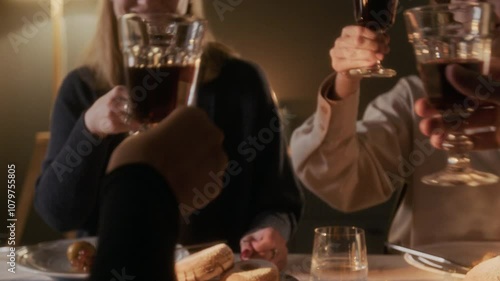 Close up view of family members clinking wine glasses in celebratory toast while sitting at festive table served with traditional Jewish meal at Hanukkah dinner in warmly-lit living room photo