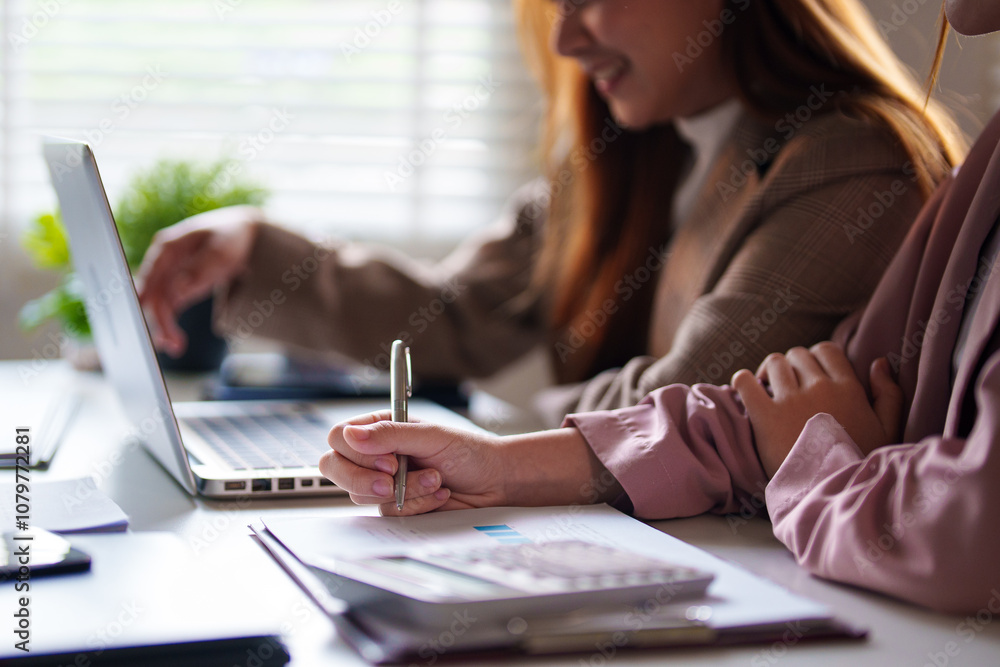 Two businesswomen sit at a desk, smiling as they look at a laptop screen. They appear engaged and pleased, suggesting a positive discussion. Two businesswomen sit at a desk, smiling as they look at a laptop screen. They appear engaged and pleased, suggesting a positive discussion.