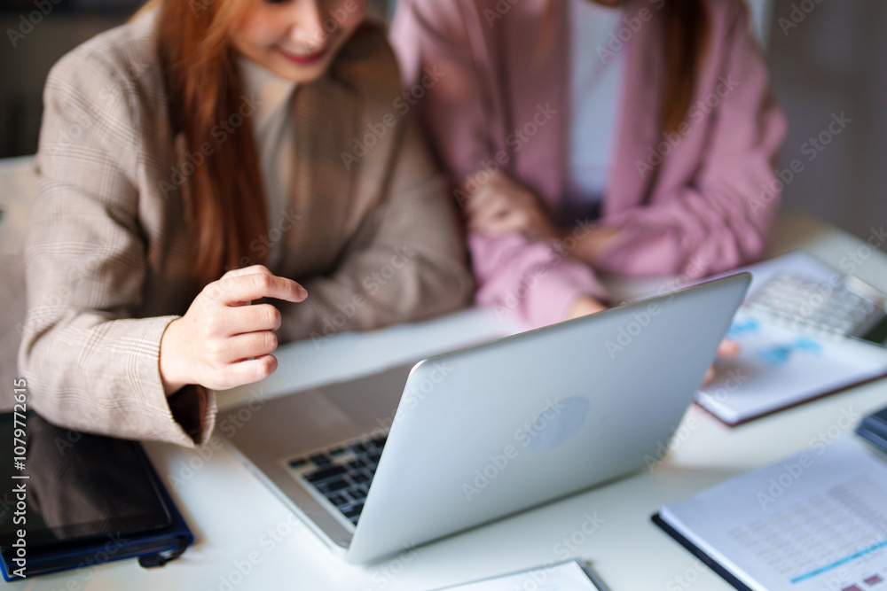 Two businesswomen sit at a desk, smiling as they look at a laptop screen. They appear engaged and pleased, suggesting a positive discussion. Two businesswomen sit at a desk, smiling as they look at a laptop screen. They appear engaged and pleased, suggesting a positive discussion.