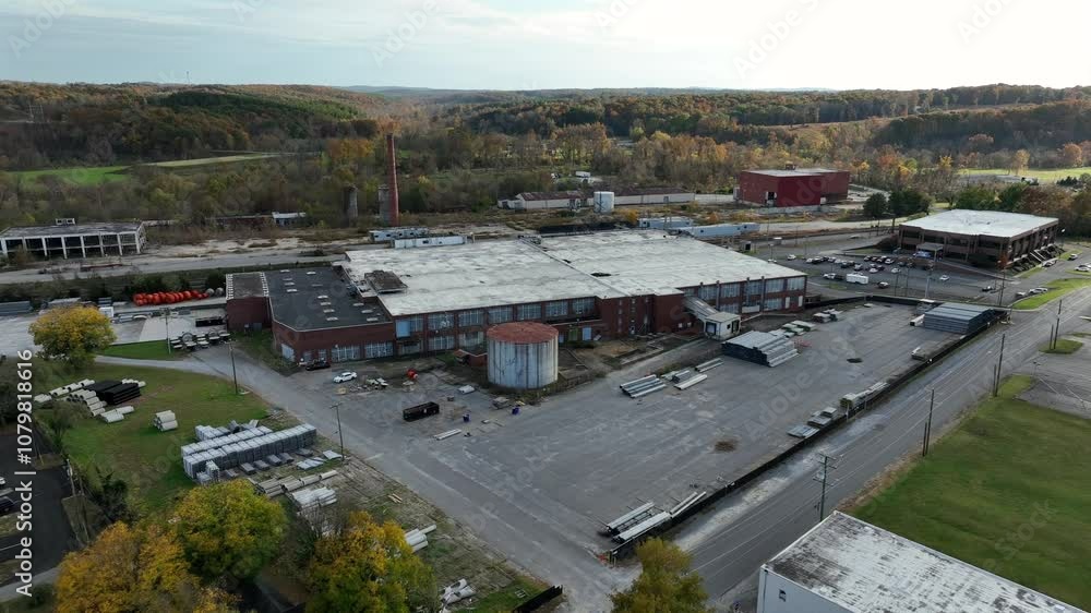 Aerial approaching shot of old rusty factory with red brick facade and smokestack. Sunny forest landscape in autumn season. Industrial suburb district in american town. Landing shot Aerial approaching shot of old rusty factory with red brick facade and smokestack. Sunny forest landscape in autumn season. Industrial suburb district in american town. Landing shot