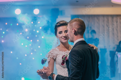 A bride and groom are dancing at a wedding reception. The bride is wearing a white dress and the groom is wearing a black suit. They are both smiling and enjoying the moment