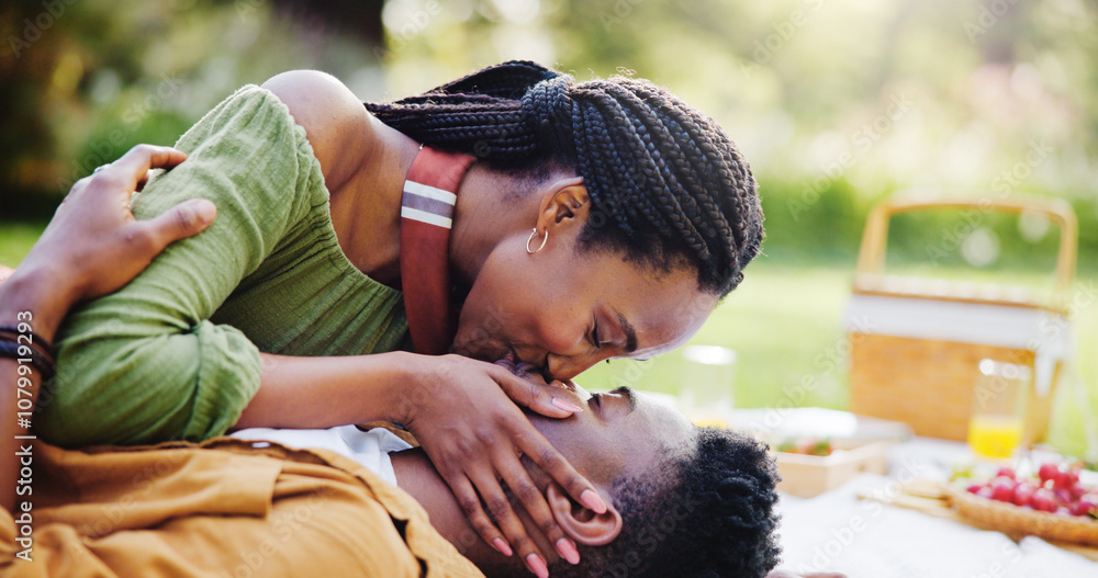 Naklejka premium Love, kiss and black couple at picnic in park for bonding, connection and outdoor adventure on happy weekend. Nature, man and woman on blanket for date together with romantic embrace, smile and trust