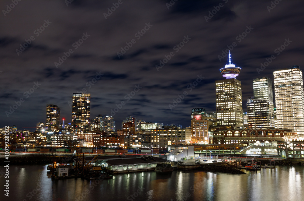 Night view of Vancouver Lookout Tower with illuminated observation deck against urban skyline, featuring waterfront buildings and port infrastructure along harbour Night view of Vancouver Lookout Tower with illuminated observation deck against urban skyline, featuring waterfront buildings and port infrastructure along harbour