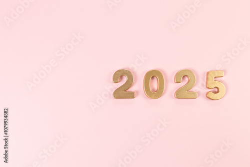 2025 Happy New Year. Top view of gold numbers on pink background. Copy space, flat lay.