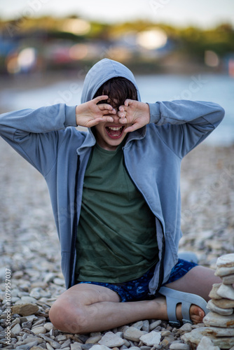 Playful boy sitting on rocky beach making funny faces photo