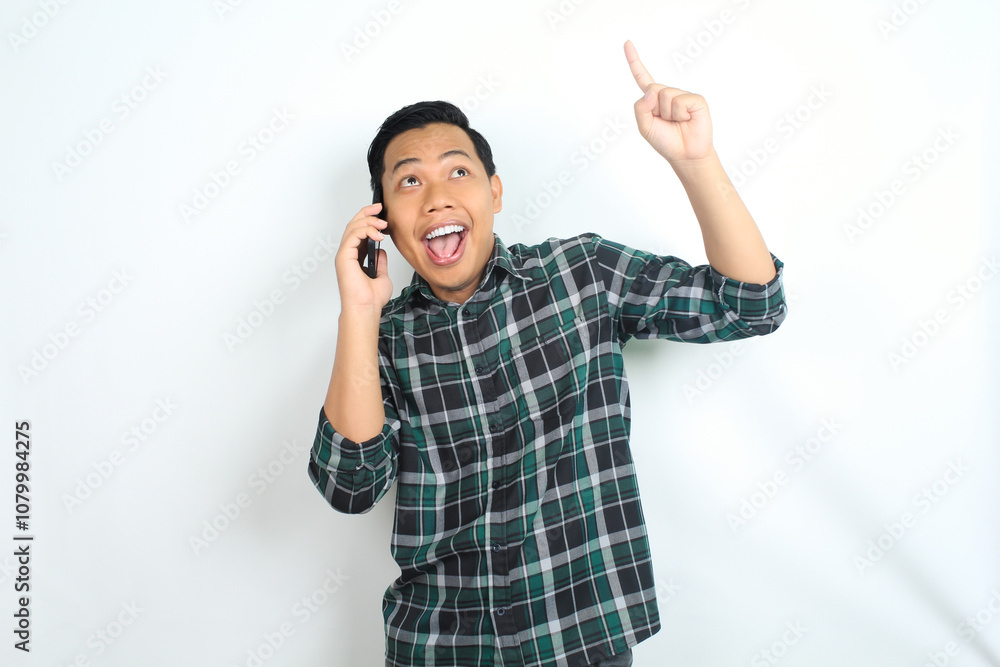 surprised asian man pointing hand while talking on smartphone isolated on white background, male wear casual green shirt