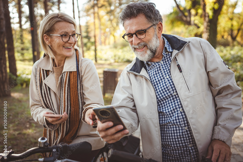 Happy senior couple walking outdoors in a park, smiling while using smartphones, enjoying technology and sharing moments together on a sunny autumn day. Happy senior couple walking outdoors in a park, smiling while using smartphones, enjoying technology and sharing moments together on a sunny autumn day.