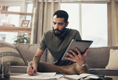 Home, man and tablet with notes for budget, track expenses and planning for financial goal on sofa. House, male person and writing with documents for payment review, digital savings or mortgage bills photo